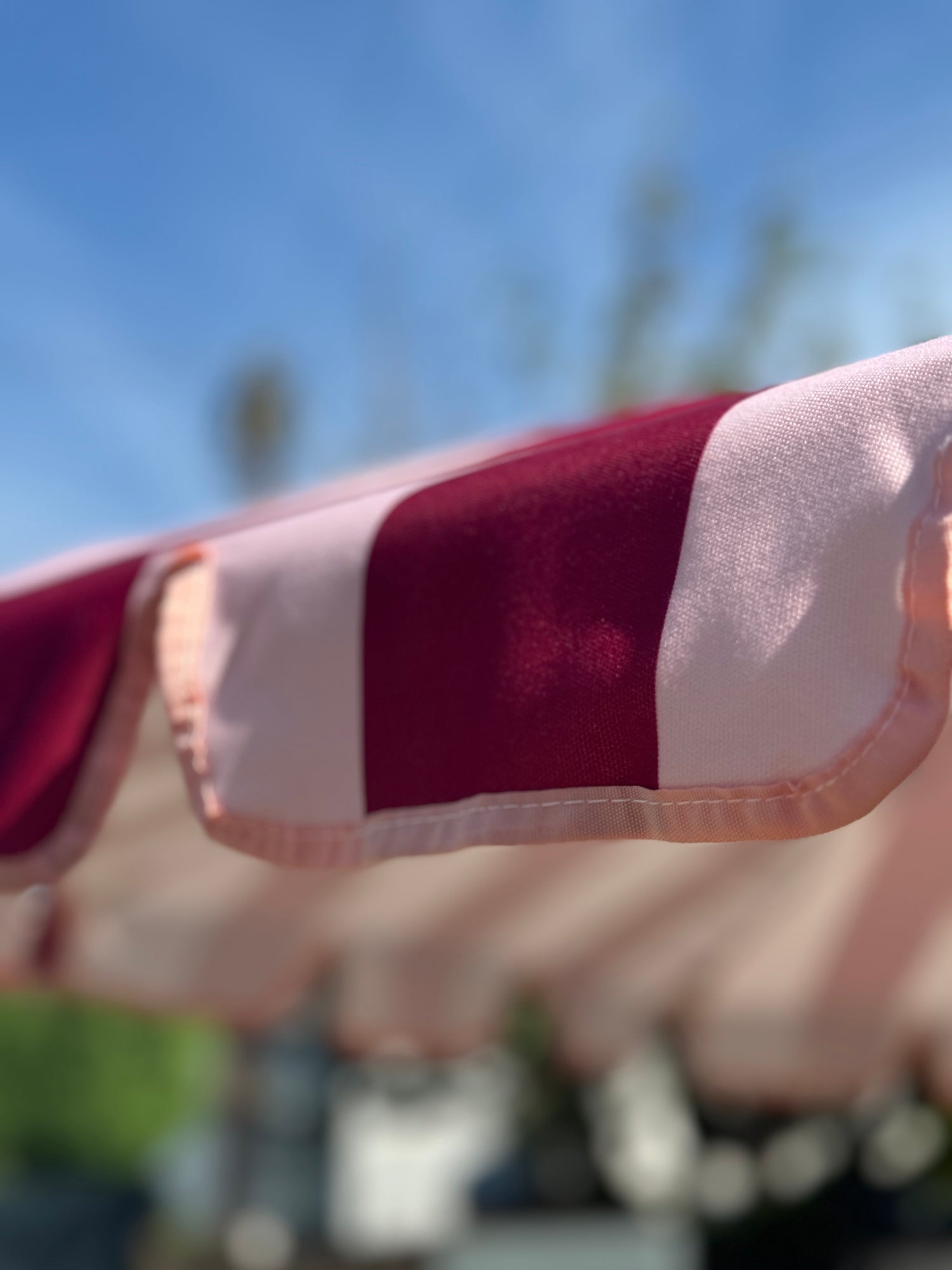 Agnes parasol with nude pink and red stripes, scallop edging, pastel pink trim, wooden frame, adjustable positioning, collapsible design, and matching canvas carry bag.