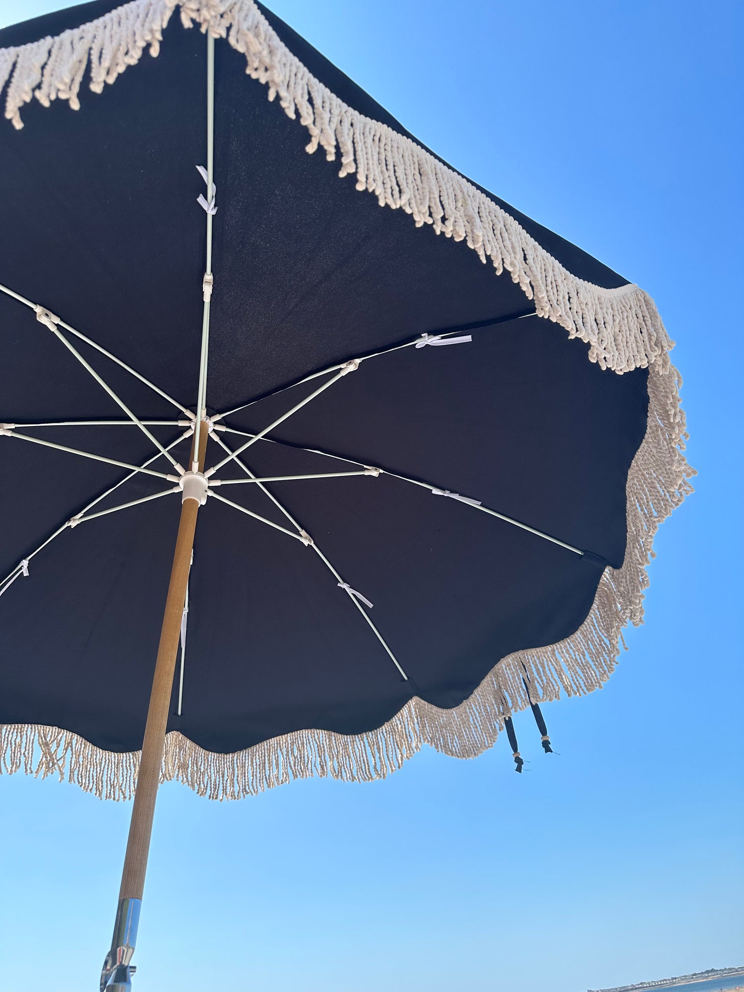 The Dorothy luxury black parasol with natural cotton fringing, wooden frame pole, adjustable positioning, collapsible design, signature logo panel, and matching carry bag."