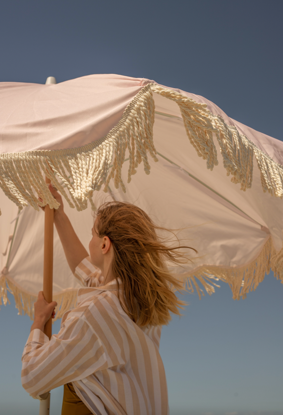 The Penelope pale pink boho chic parasol with natural cotton fringing, adjustable wooden frame pole, collapsible design, and matching canvas carry bag.