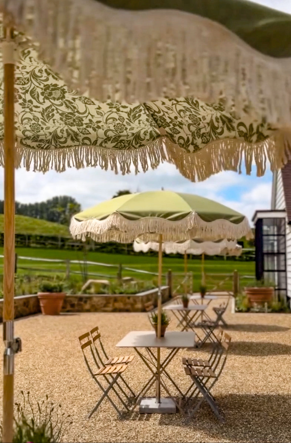 Bridget olive green parasol with natural cotton fringing, floral inner pattern, wooden frame, adjustable positioning, collapsible design, and matching canvas carry bag.