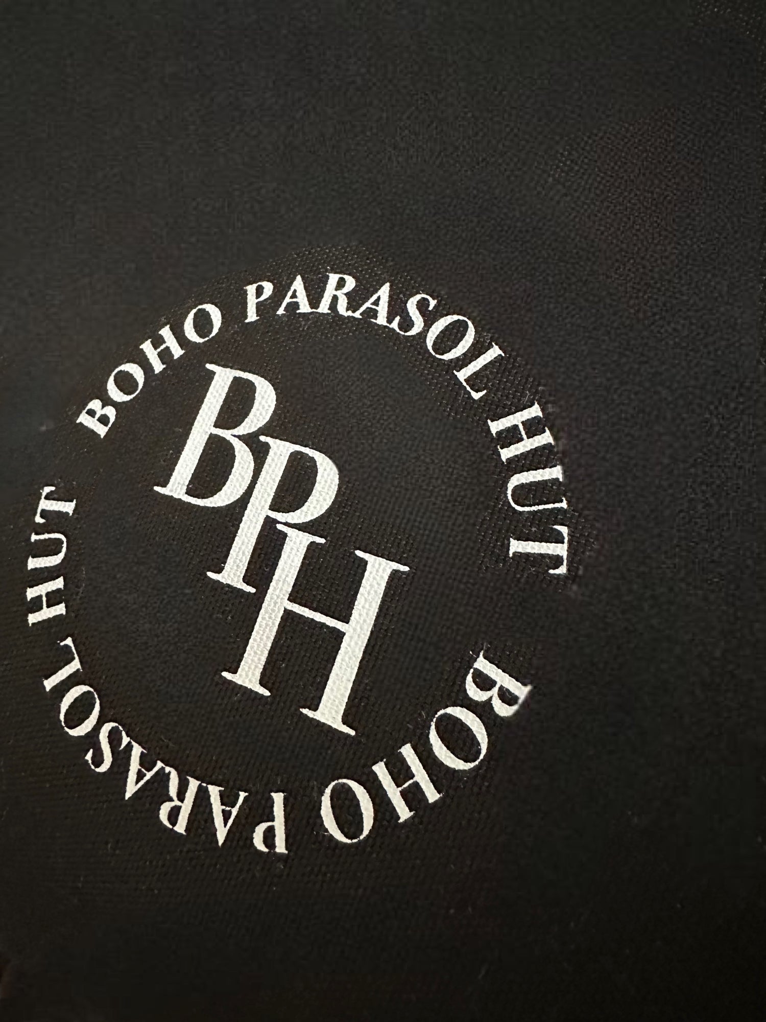 The Dorothy luxury black parasol with natural cotton fringing, wooden frame pole, adjustable positioning, collapsible design, signature logo panel, and matching carry bag."