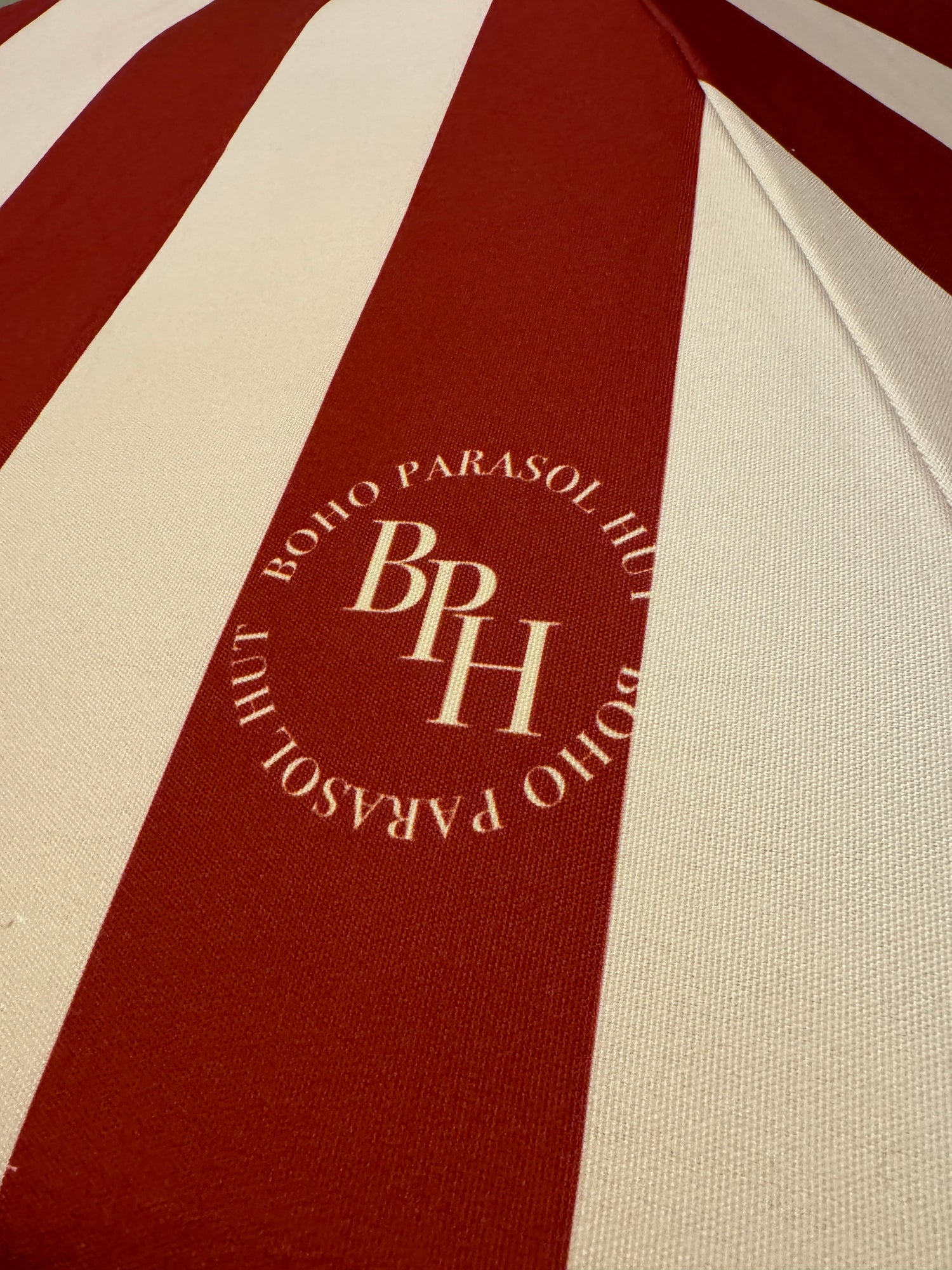 Agnes parasol with nude pink and red stripes, scallop edging, pastel pink trim, wooden frame, adjustable positioning, collapsible design, and matching canvas carry bag.