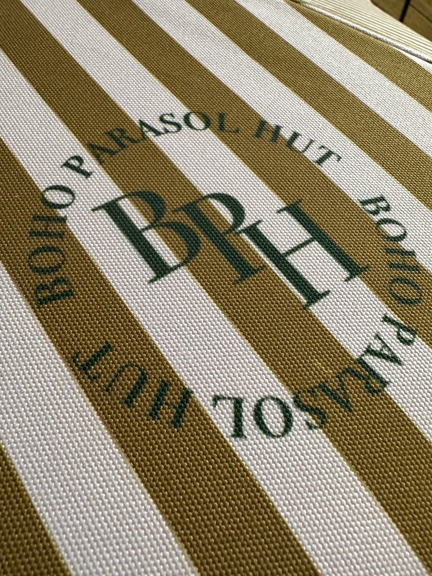 The Gigi luxury pink and camel striped parasol with natural cotton fringing, wooden frame pole, adjustable positioning, collapsible design, and matching carry bag.