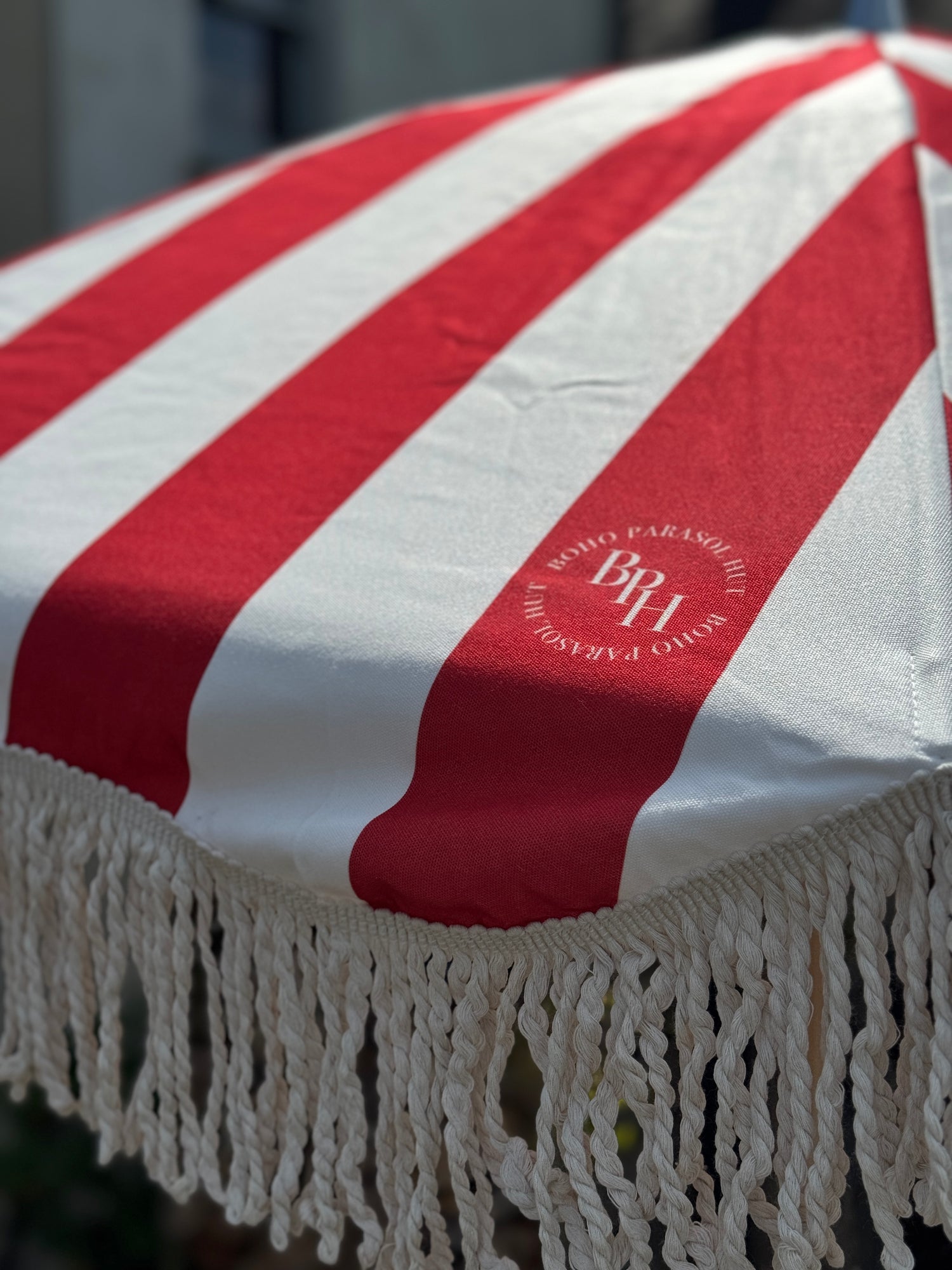 Harry parasol with red and white stripes, natural cotton fringing, wooden frame, adjustable positioning, and matching canvas carry bag.