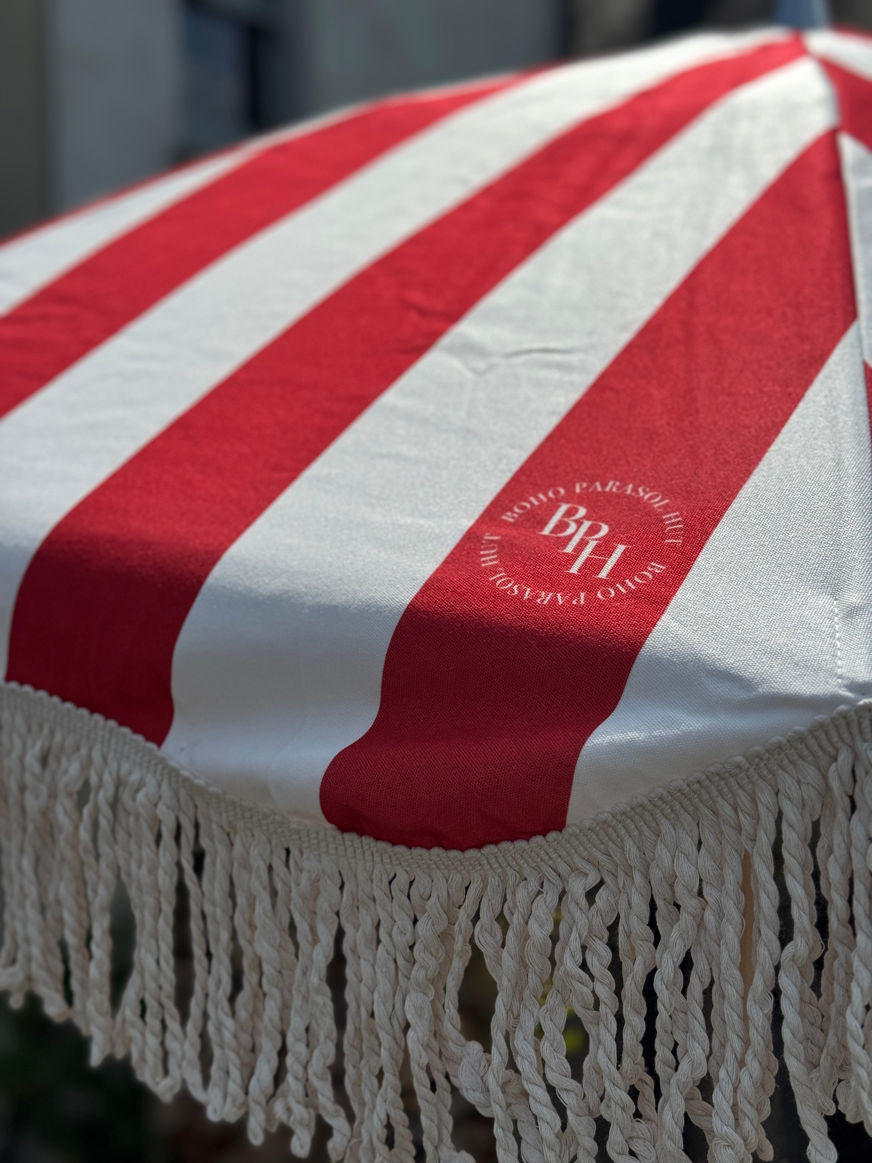 Harry parasol with red and white stripes, natural cotton fringing, wooden frame, adjustable positioning, and matching canvas carry bag.