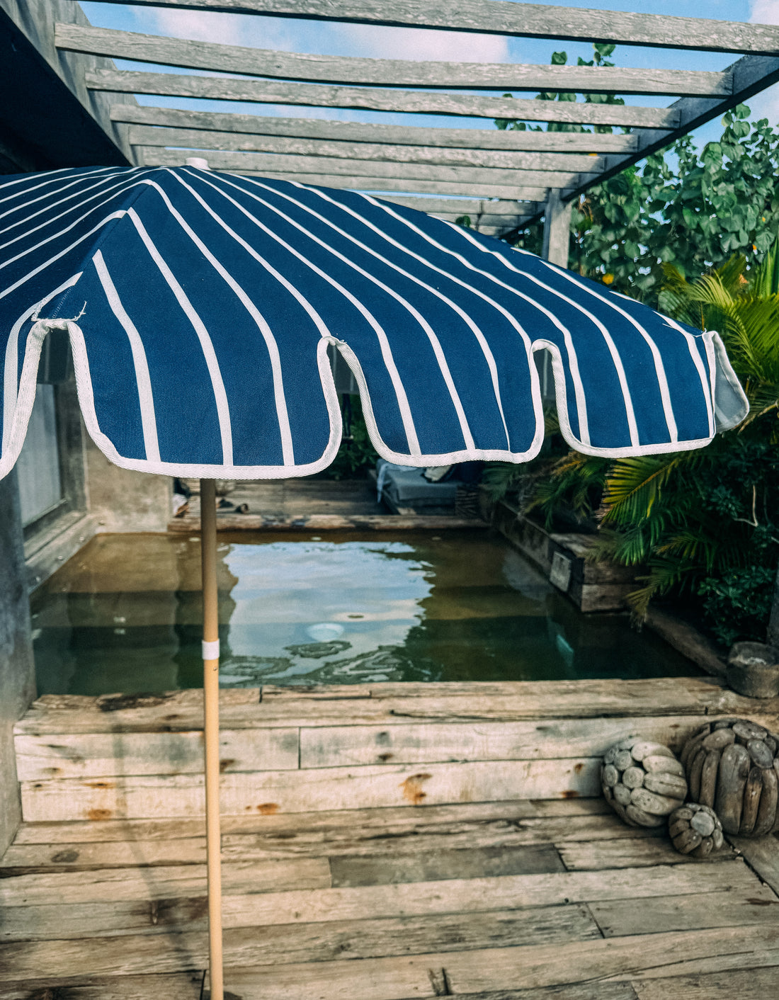 Chic Matilda navy and white striped scallop parasol at a poolside, offering stylish shade by the water on a sunny day.