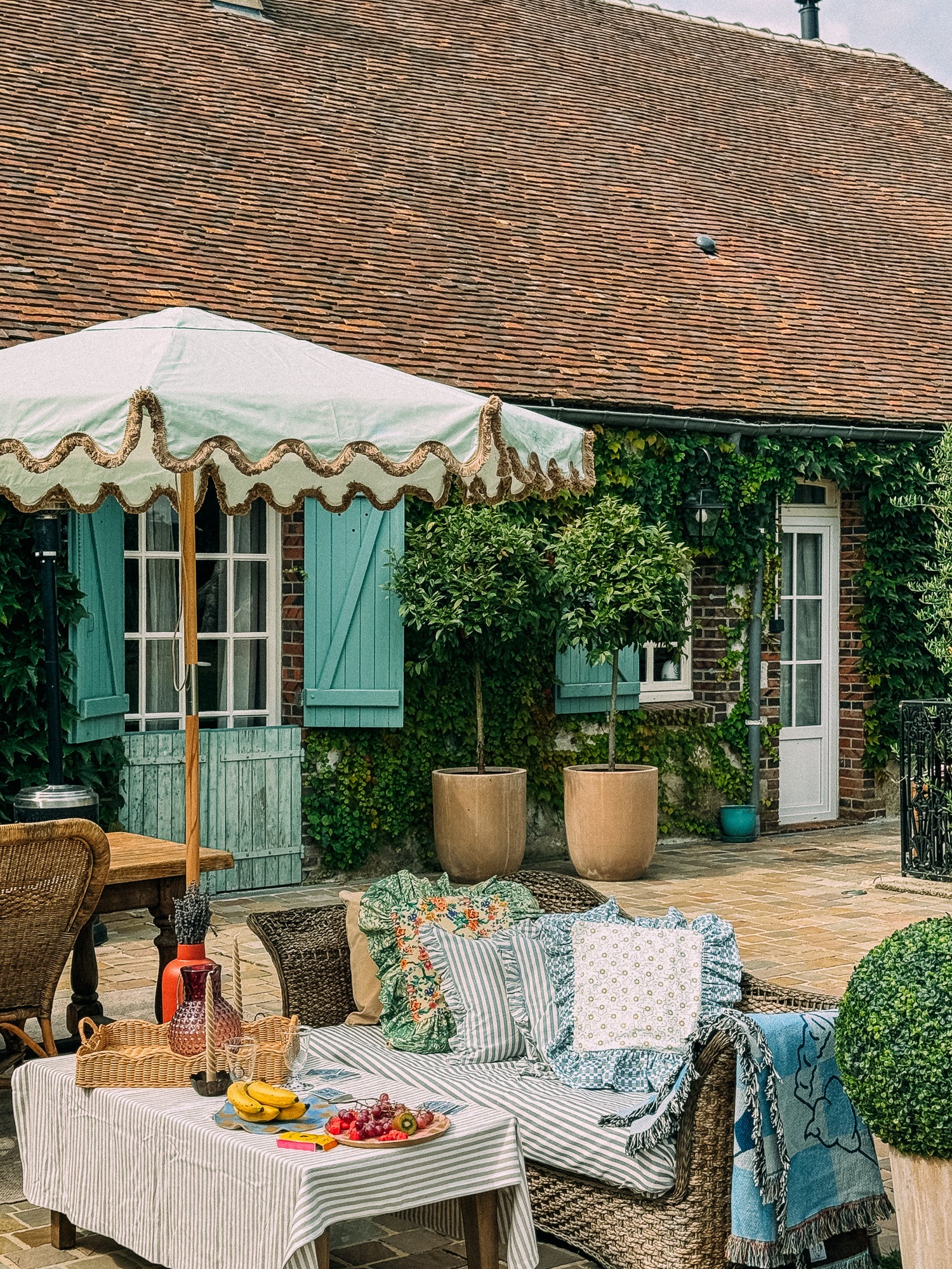 Willow green parasol with brown fringing, set on a patio with a stylish tablescape dinner setting, creating an elegant outdoor dining atmosphere.