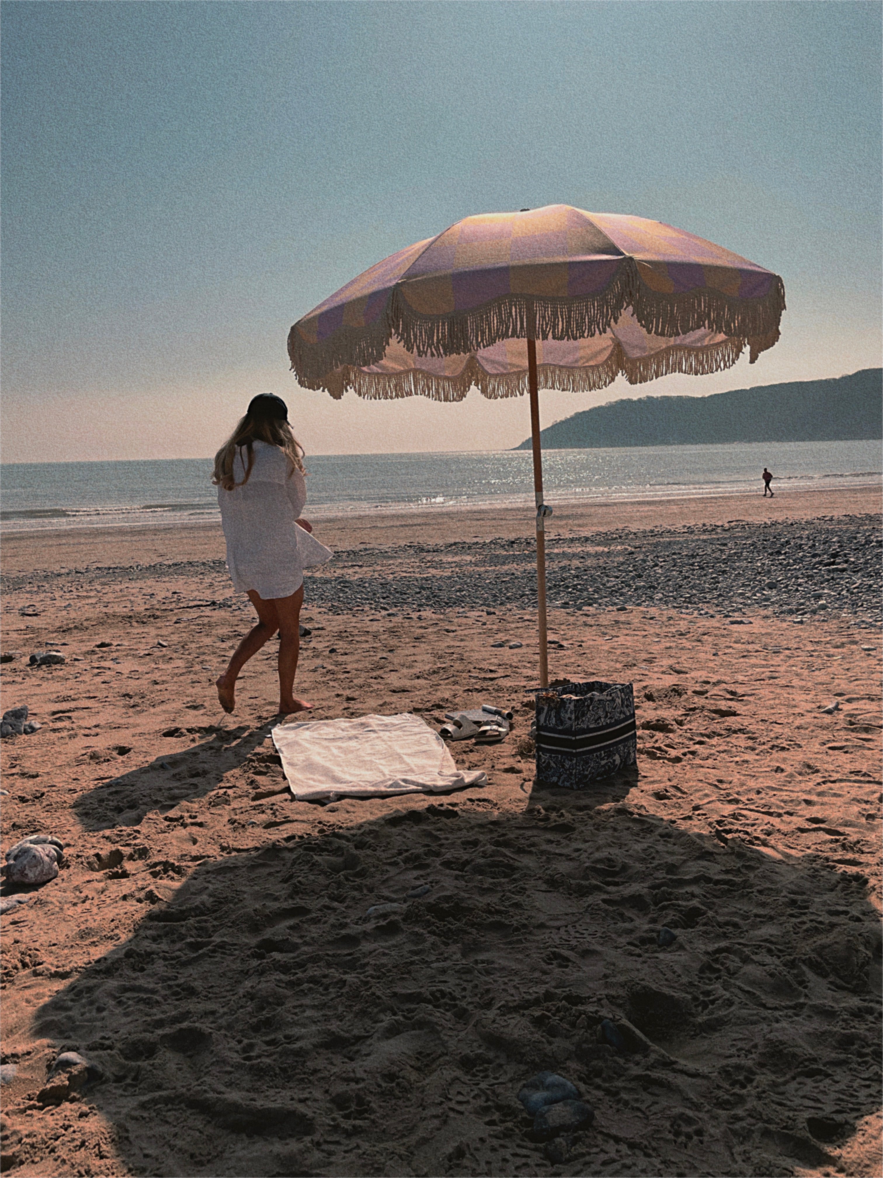 The Mabel boho chic parasol with lilac and cream checkerboard print, natural cotton fringing, adjustable wooden frame pole, collapsible design, and matching canvas carry bag.