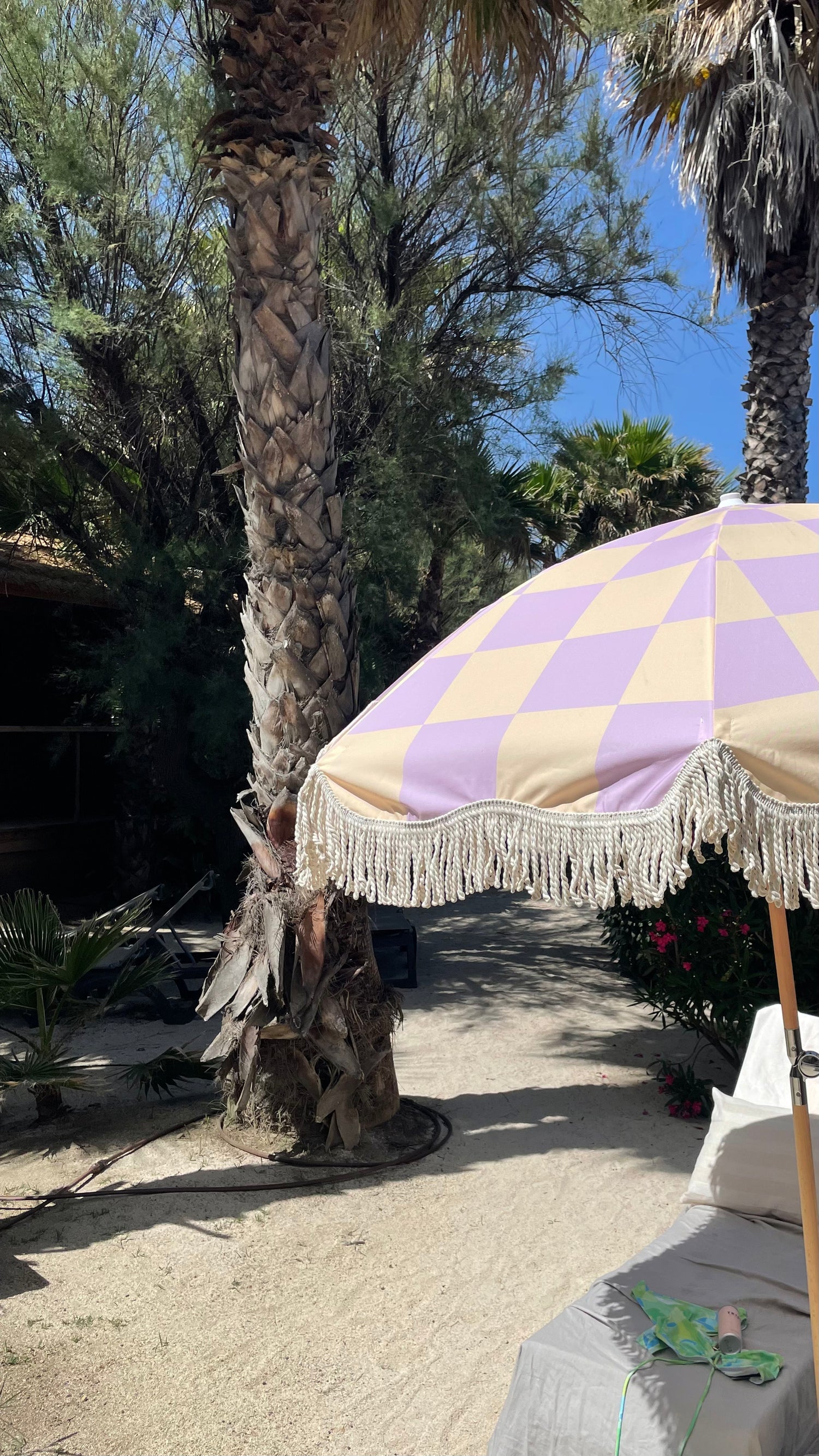 The Mabel boho chic parasol with lilac and cream checkerboard print, natural cotton fringing, adjustable wooden frame pole, collapsible design, and matching canvas carry bag.