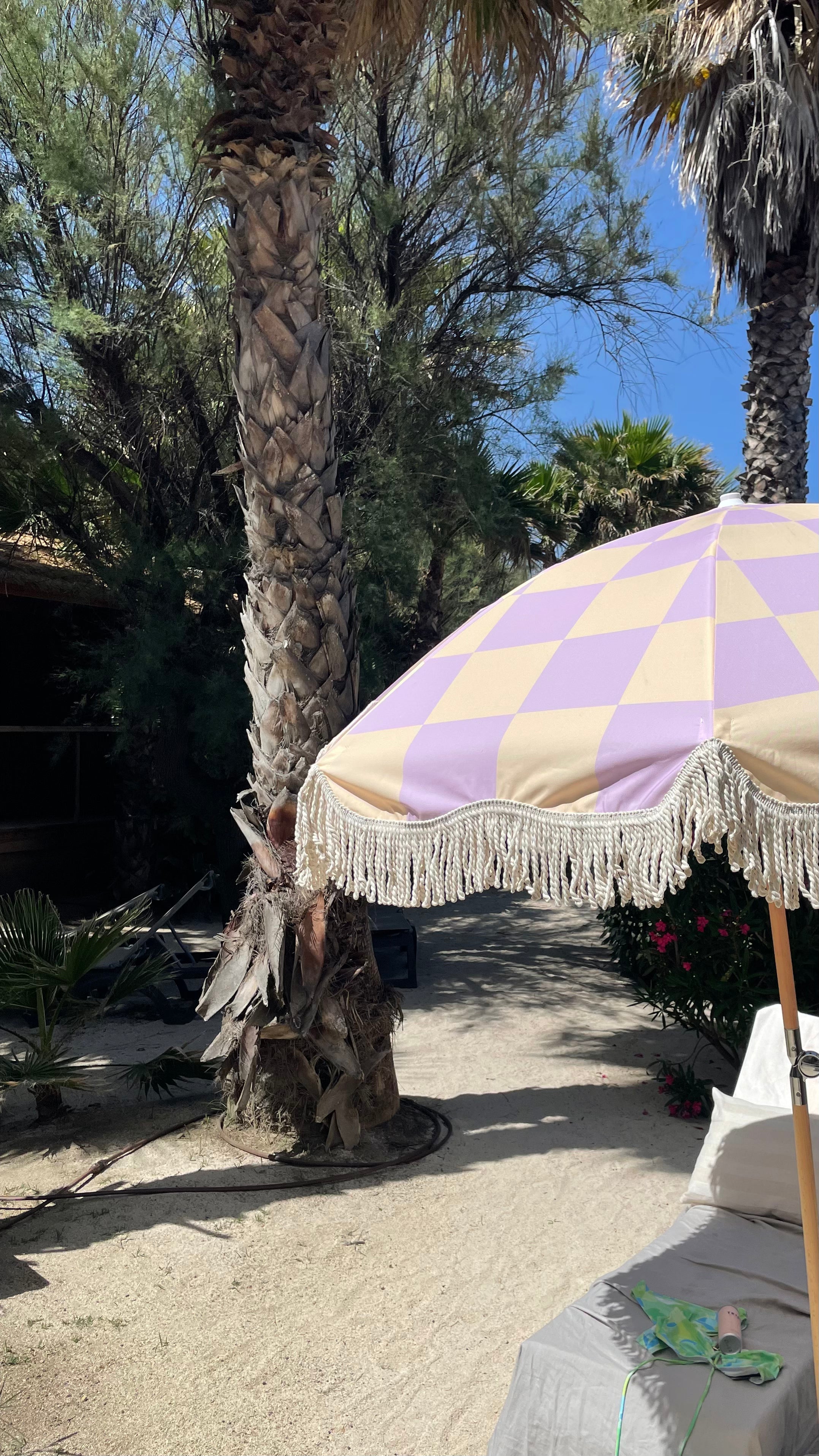 The Mabel boho chic parasol with lilac and cream checkerboard print, natural cotton fringing, adjustable wooden frame pole, collapsible design, and matching canvas carry bag.