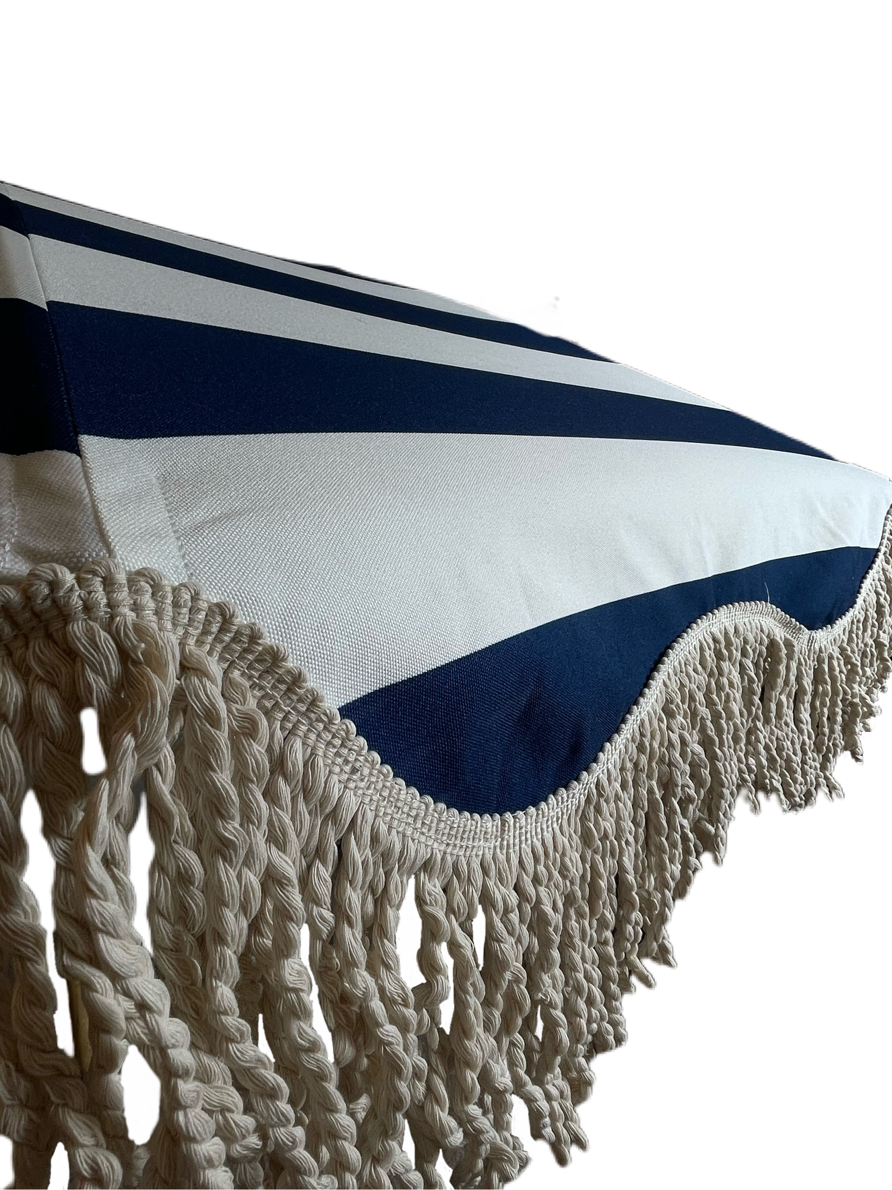 The Hugo timeless chic parasol with natural cotton fringing, wooden frame pole, adjustable positioning, collapsible design, and matching canvas carry bag.