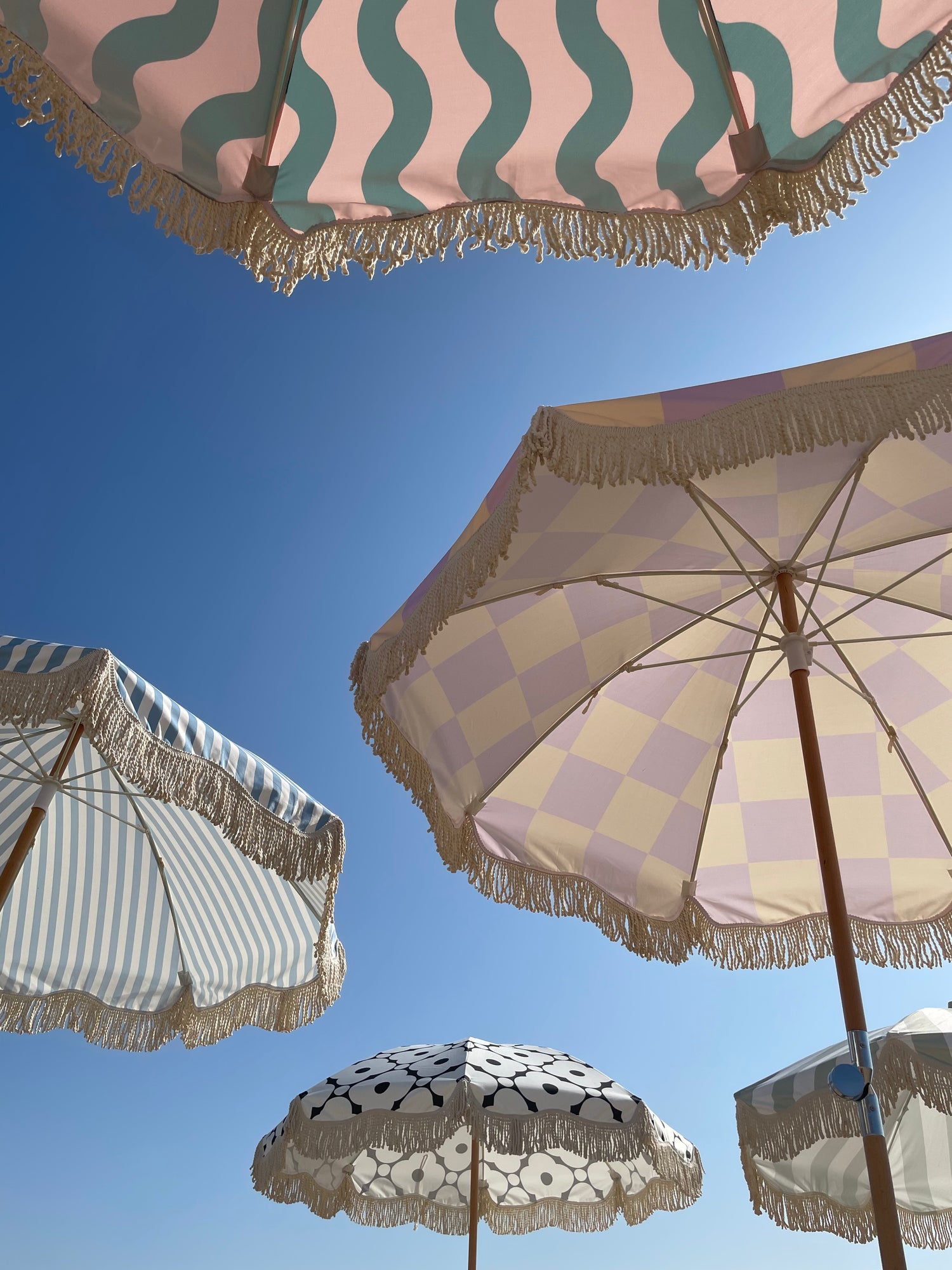 The Mabel boho chic parasol with lilac and cream checkerboard print, natural cotton fringing, adjustable wooden frame pole, collapsible design, and matching canvas carry bag.