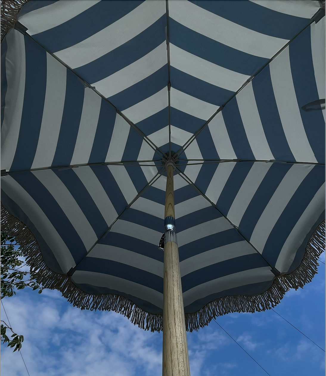 The Hugo timeless chic parasol with natural cotton fringing, wooden frame pole, adjustable positioning, collapsible design, and matching canvas carry bag.