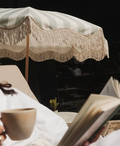 Sage green striped parasol with fringed edge styled outdoors