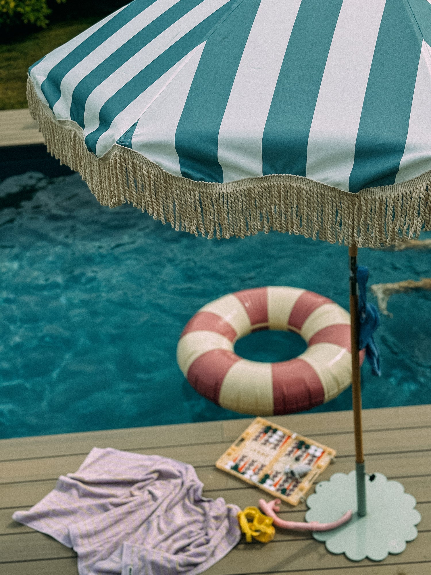 British-made blue striped parasol with fringe styled poolside alongside outdoor accessories